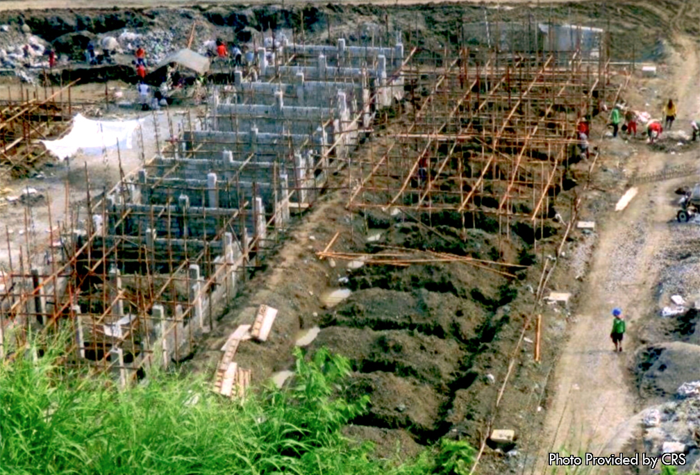 The associated picture was taken outside one of the construction sites were the houses are being built. On the right side of the photo is what the beginning stage looks like. The workers have begun to dig the foundation for the houses. In addition, they have also begun to place wood into the shape of the houses. To the left side of the photo you can see the next stage of the building process. Here the cement is being put into the skeleton of the house. After some time has passed these houses will be built and the 900 families will be able to live without having to worry. To ensure that the newly built community will continue to strive even after the CRS has left, a home owner association will be put into place.
