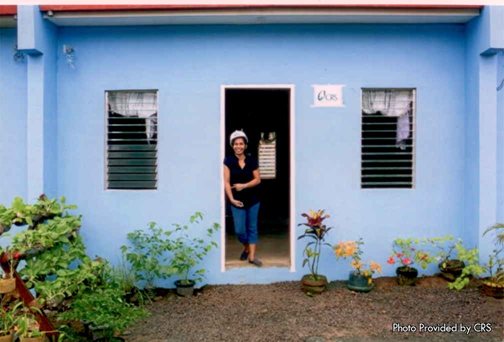 A builder happily stands in the front door of her finished home.