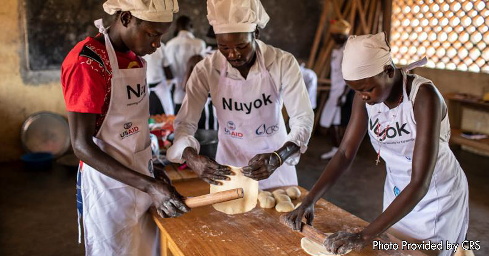 Will Baxter from the Catholic Relief Services captures a moment of young adults involved in the program. The young adults are using the skills and training that they received to roll out dough to make some chapatis. Chapatis is an unleavened bread made from wheat flour and water. The baking class is part of a vocational training initiative.