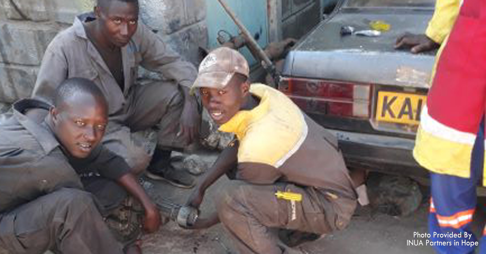Three men work on repairing a car.