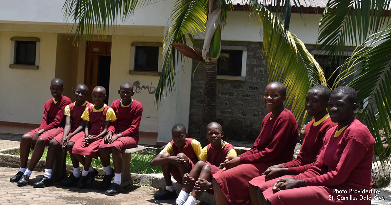 Children in their school uniforms sit outside the homes.