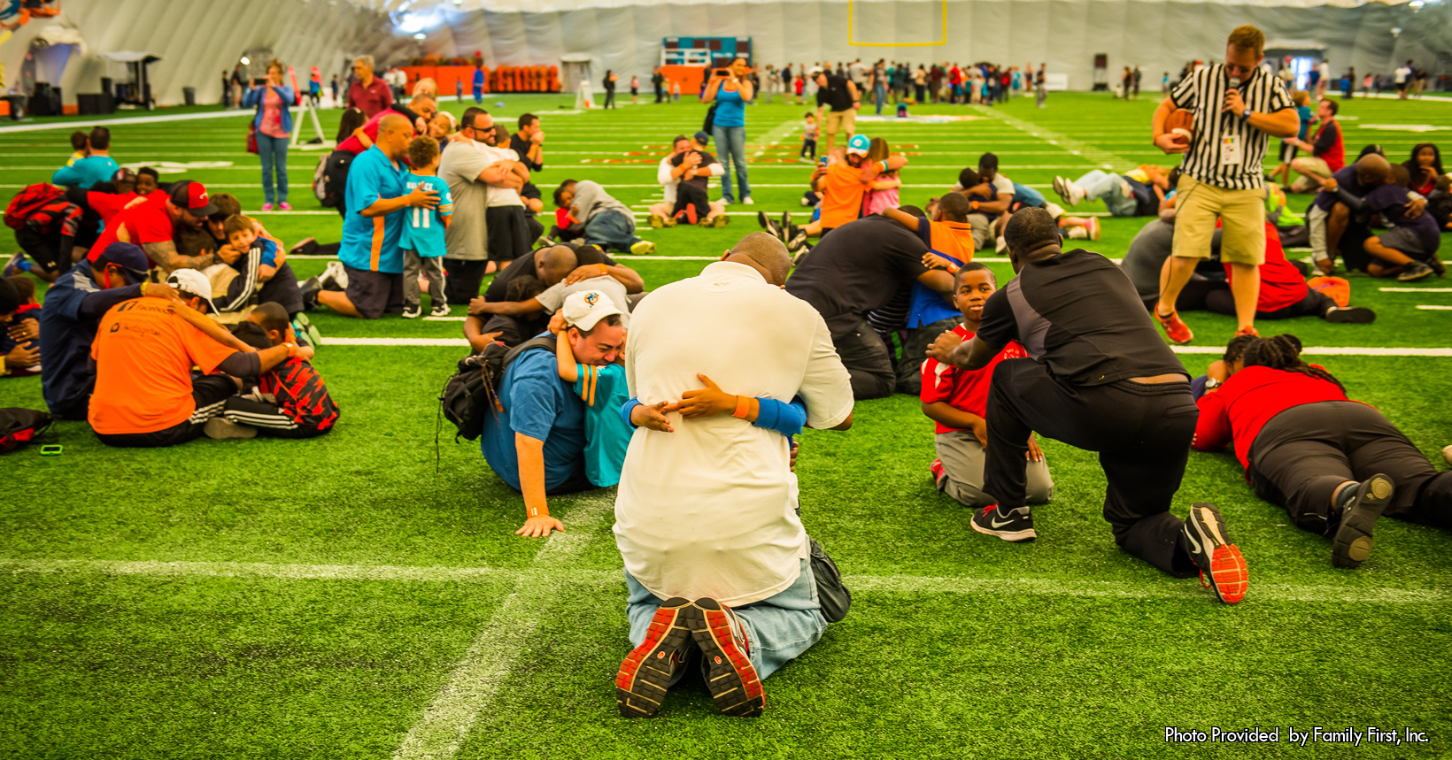 Children and adults talk and hug after an event on a football field.
