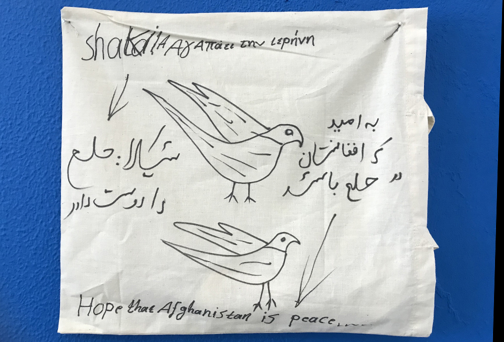 A child’s flag posted in a hub lobby as part of an art instalation.  Shakdia asks in three languages for peace in Afghanistan centered around two doves.