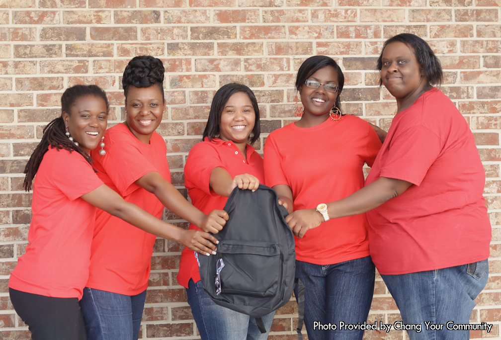 This photo was taken outside next to a brick wall. Given to the Father's Table foundation by the Change Your Community program, this picture shows five ladies posing for the picture. Every one of the ladies in the photo is wearing a red short sleeved shirt with long pants. Four out of the five ladies are wearing blue jeans while the lady to the far left is wearing black jeans. Every one of the ladies are smiling in the photo because they are serving a cause that is bigger than all of them. They are willing to help out less fortunate kids who don’t have access to the same supplies other kids have. As a matter of fact, the backpack that all of the ladies in the photo are holding is the solution to the problem. The Change Your Community is providing school supplies to the less fortunate kids. In the backpack are several school supplies that are required of students to have when they go to class. To start off, some of the backpacks will be packed with pencils and pens. The pencils and pens will be used by the students to write in their planners to keep themselves organized. In addition, the pens and pencils will be used to take notes on what they are learning as well as to do their homework. Furthermore, the backpacks can come with paper that will be written on by the pencils and pens. With all of these supplies in the backpacks, parents who couldn’t afford to buy their kids school supplies don’t have to anymore. They will be able to rest in the fact that the Change Your Community took it upon themselves to help them out. With this, the parents can rest knowing that their kids will be fully equipped when they go to school.