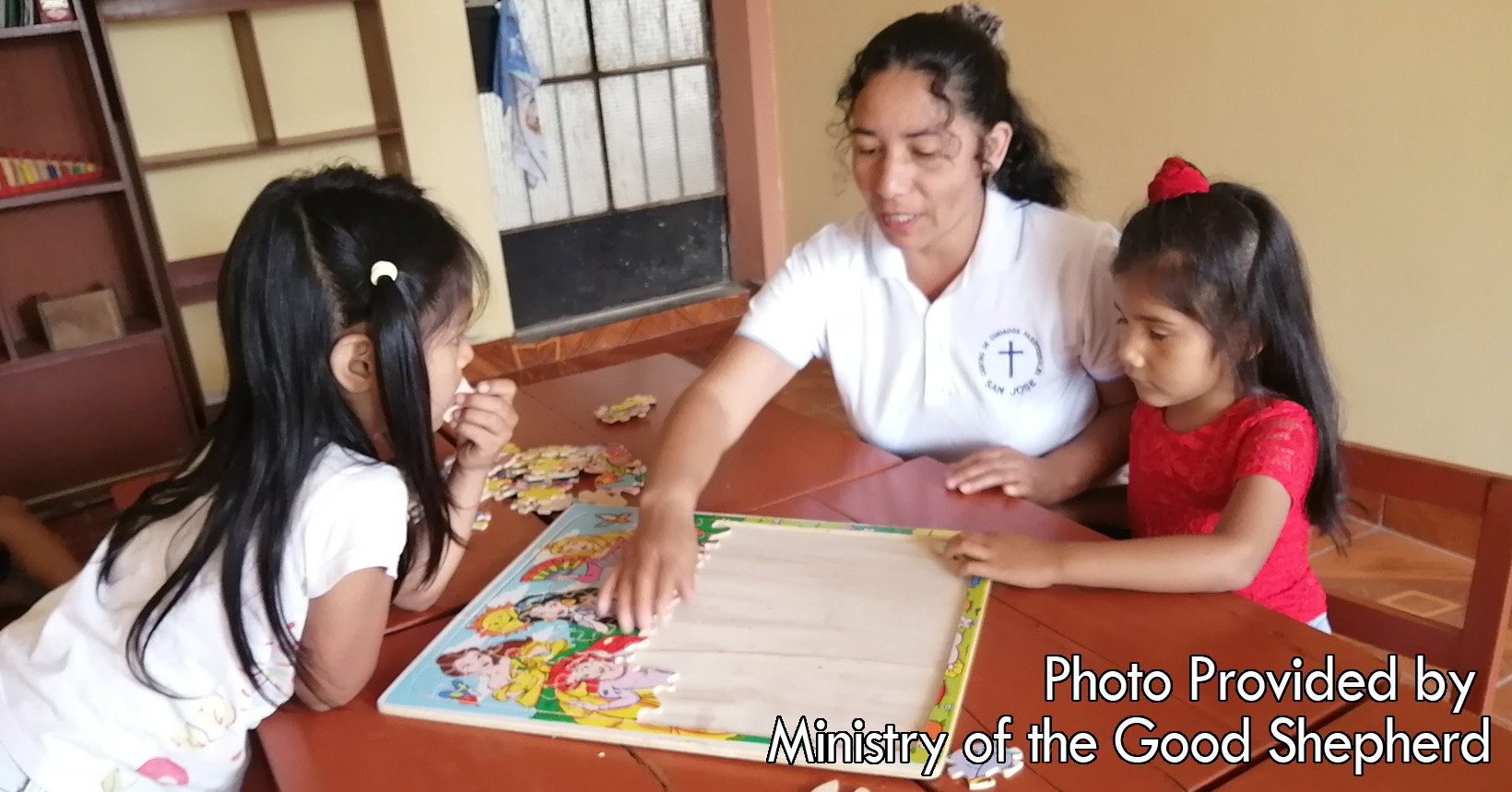 One of the sisters is helping two young girls solve a puzzle. The two girls are learning how to put things together which will help them further in life.