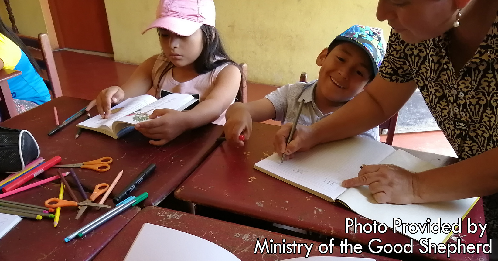 A sister from The Ministry of The Good Shepard is going around and helping the young kids with their work. The children are reading and writing as they wait to go home later in the day.
