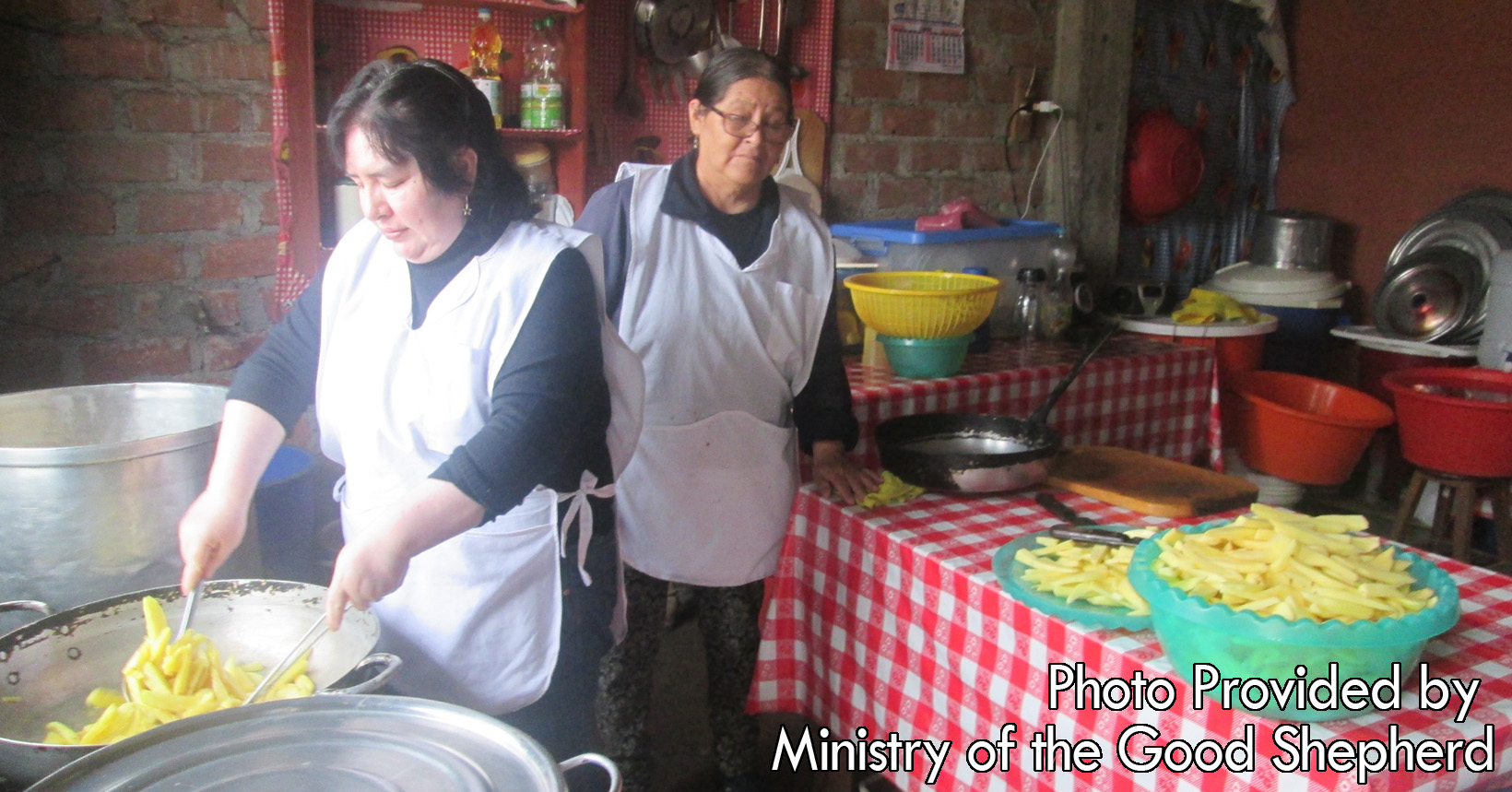 Two ladies in the kitchen are preparing a meal for the young kids. Wearing their aprons, they are preparing some pasta with all the utensils available to them.